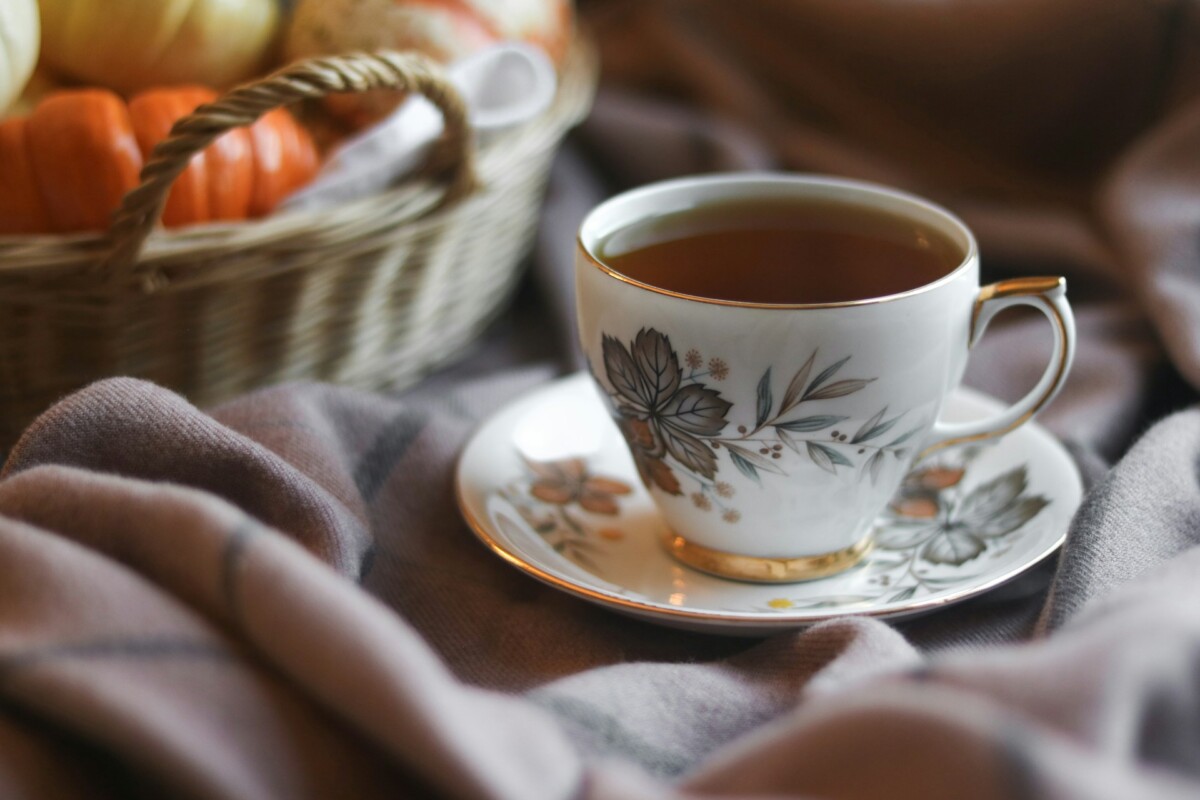 china tea cup with basket of gourds in background and cozy blanket in foreground