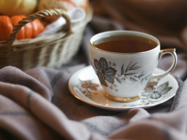 china tea cup with basket of gourds in background and cozy blanket in foreground