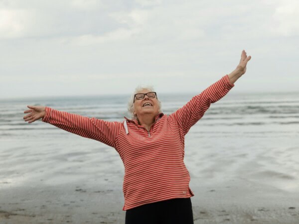 Mature woman with arms outstretched with ocean behind her
