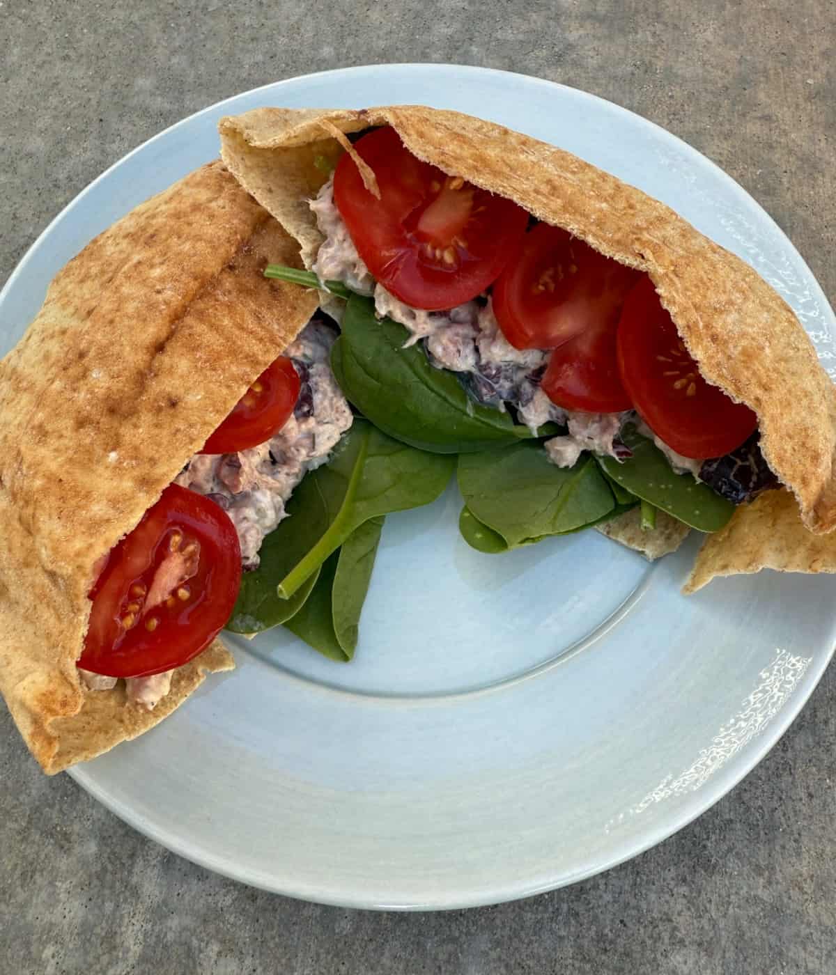 Greek Tuna Salad stuffed pita bread pocket with spinach and tomato slices on blue plate.