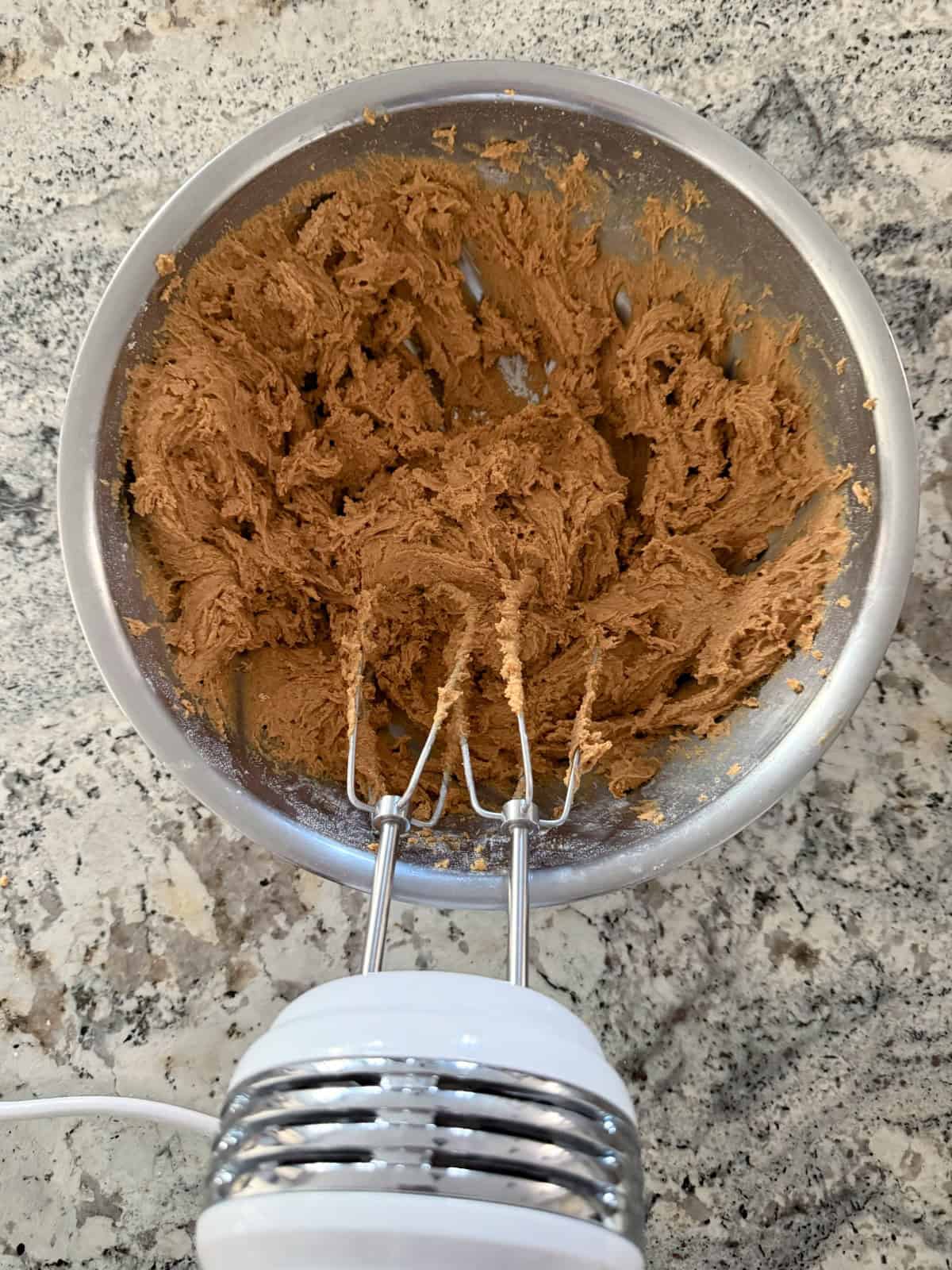Using electric hand mixer to beat ginger cookie dough in mixing bowl.