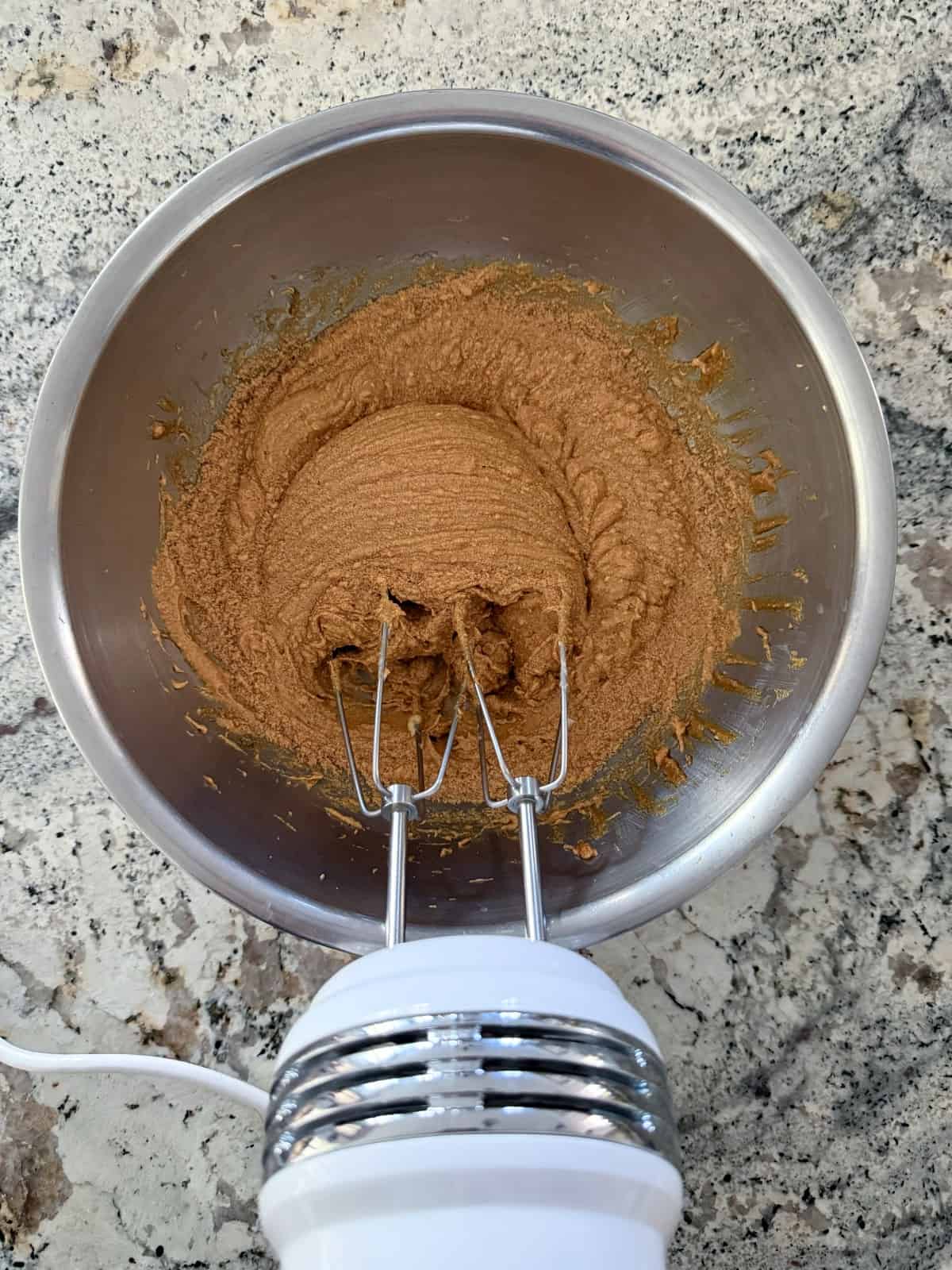 Beating molasses, butter and no calorie sweetener with an electric hand mixer in mixing bowl.