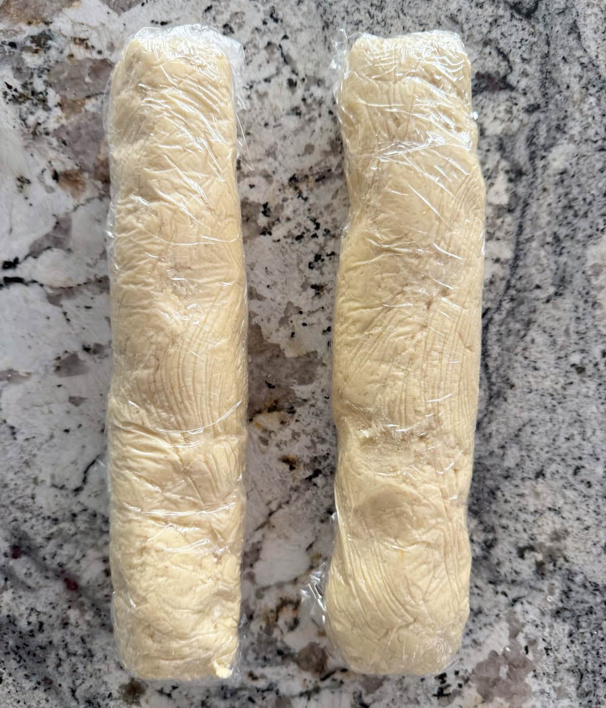 Two shortbread cookie dough logs wrapped in plastic wrap.