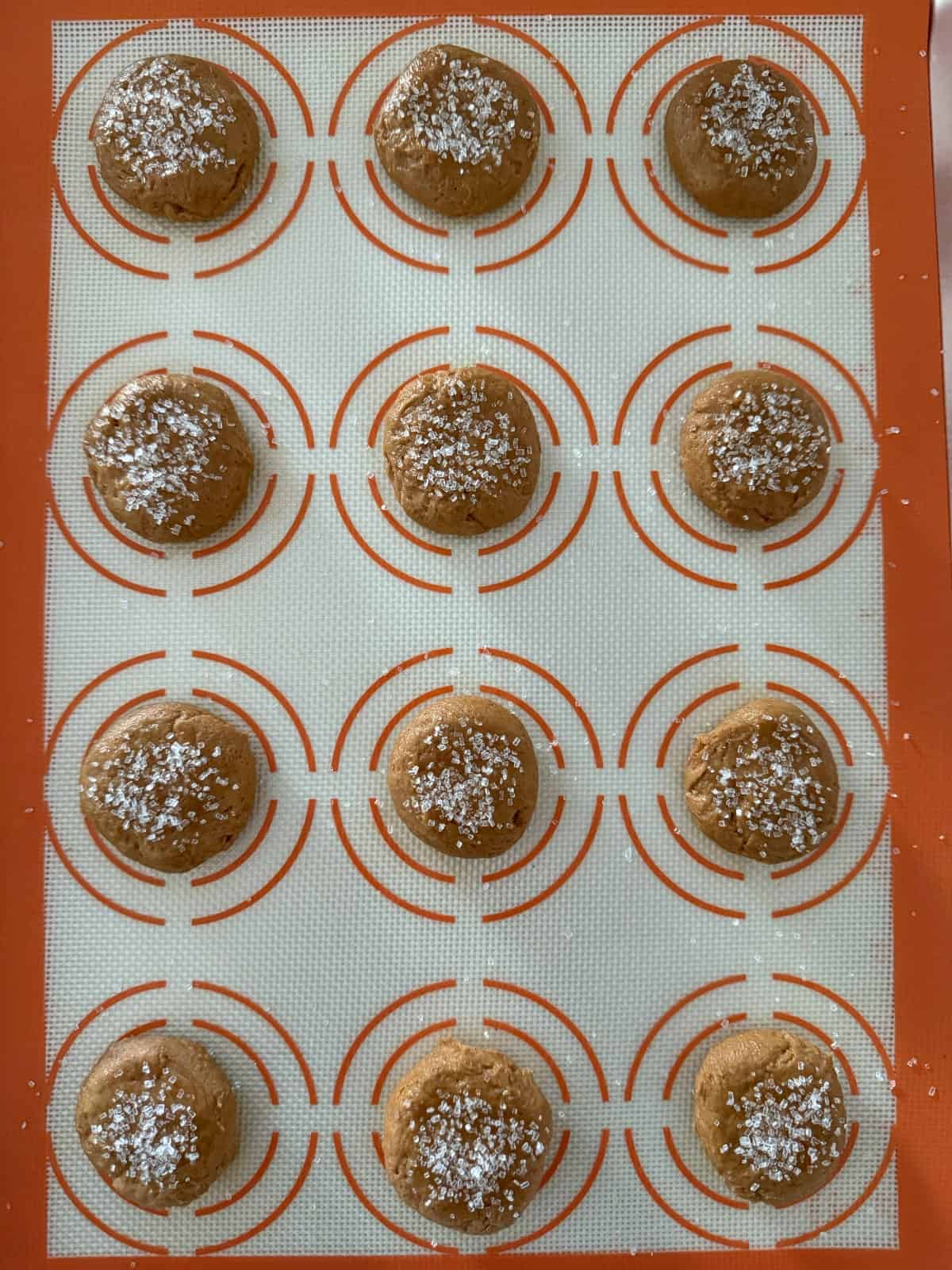 Unbaked ginger cookies sprinkled with sparkling sugar on silicon lined cookie sheet.