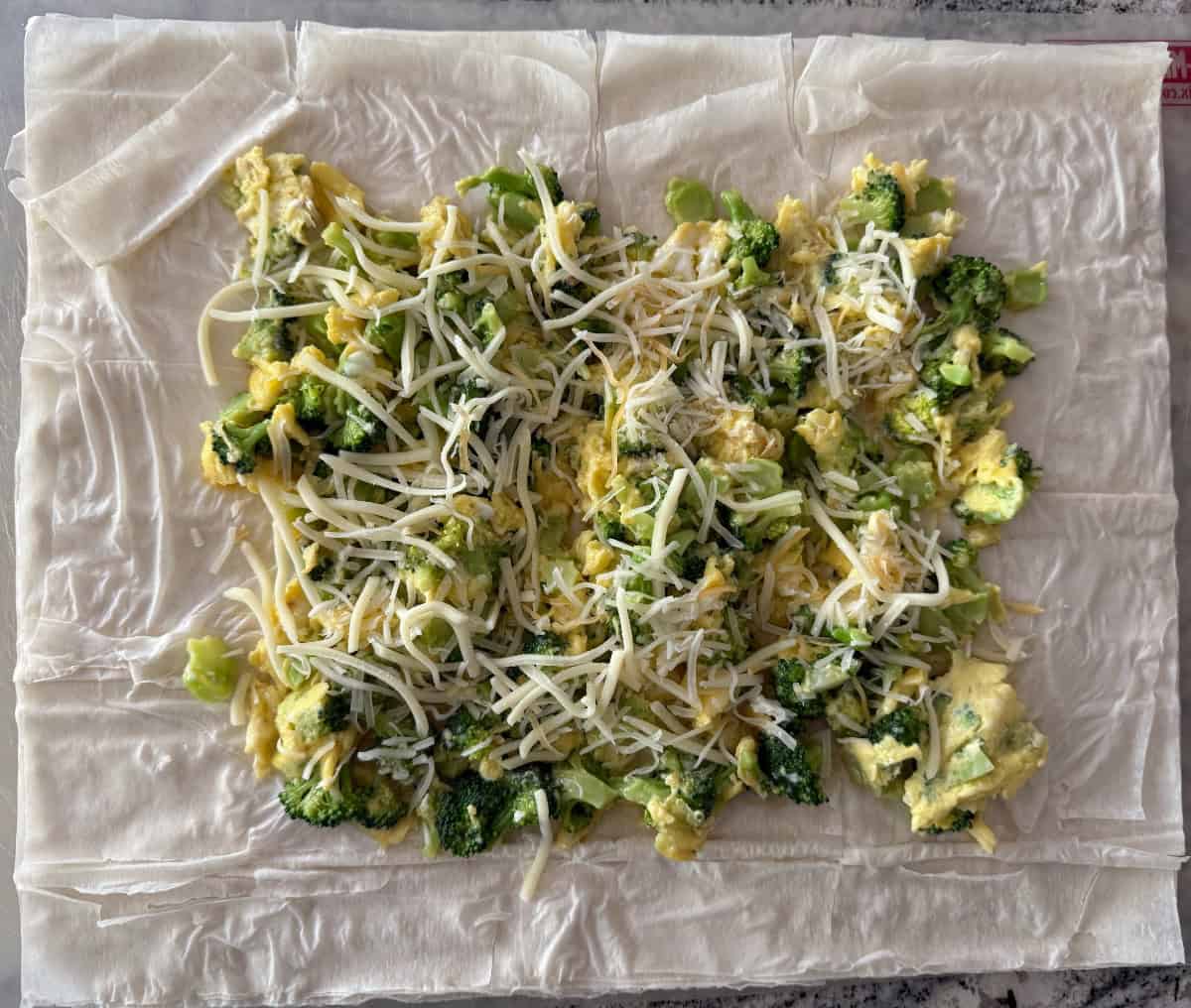Scrambled eggs with broccoli and shredded cheese on phyllo dough pastry sheets.