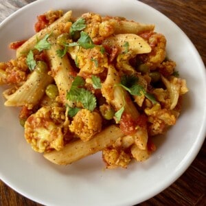 curried cauliflower pasta garnished with cilantroon a white plate shot from above