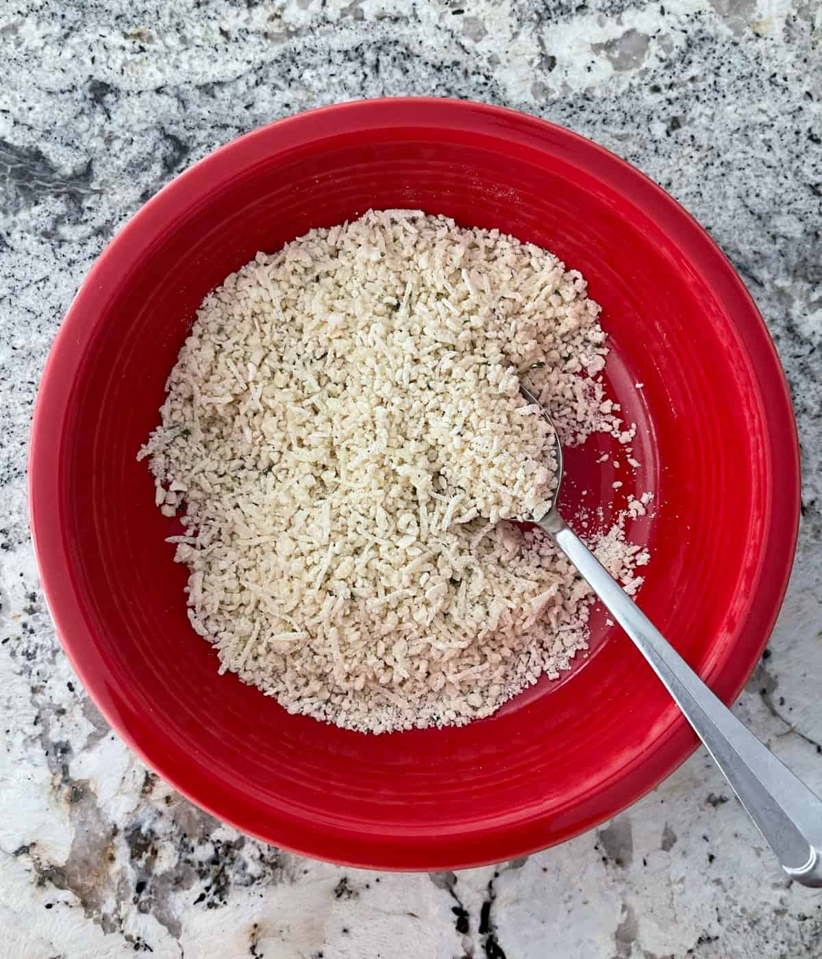 Mixing Panko bread crumbs, grated Parmesan cheese and dry ranch seasoning in red bowl with a spoon.
