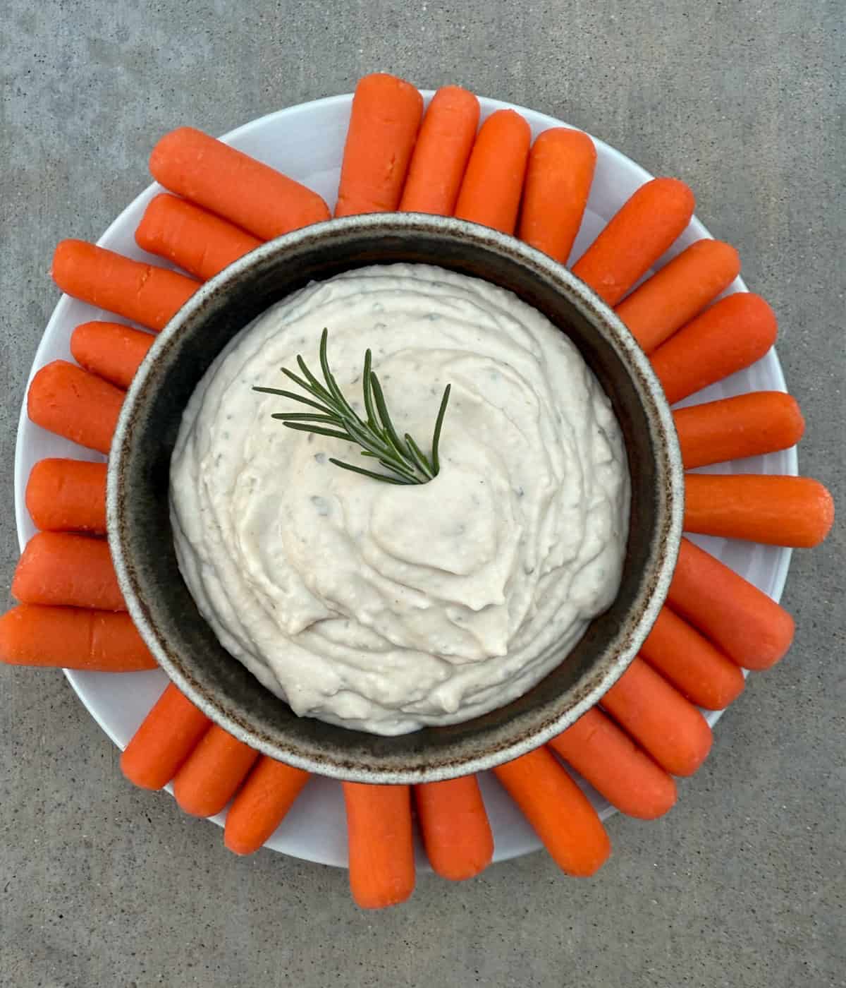 Tuscan White Bean Dip in a small bowl with a plate of carrot sticks.