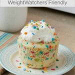 whipped topping topped funfetti mug cake on colorful plate in front of mug and microwave
