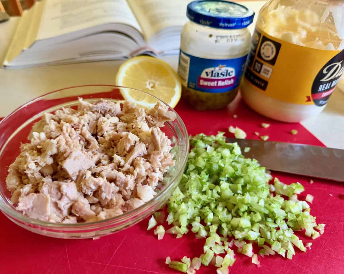 Ingredients for Tuna Salad - Drained tuna, finely diced celery on cutting board, 1/2 fresh lemon, jar of pickle relish, jar of mayonnaise