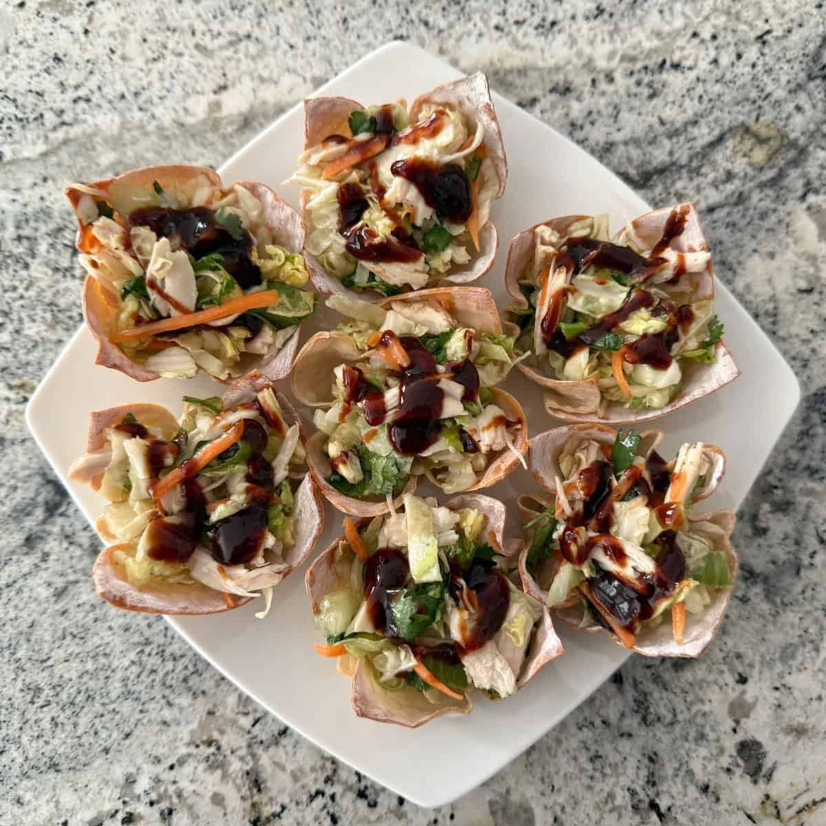 Asian chicken salad wonton cups on square white plate.