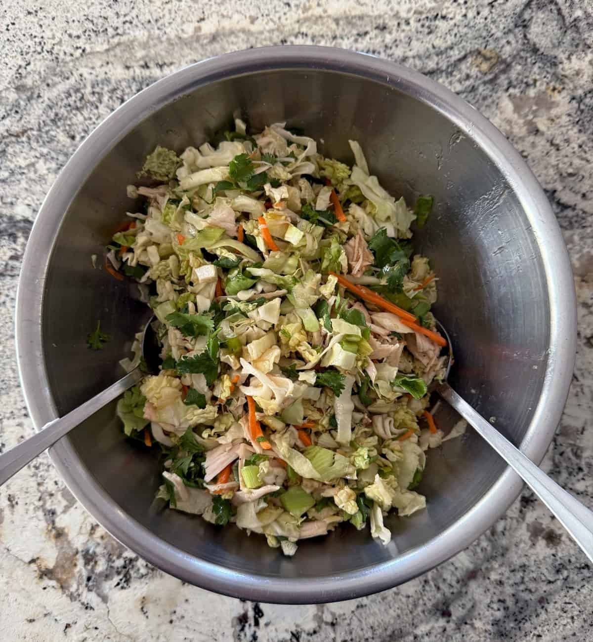 Tossing Asian chopped salad in mixing bowl with spoons.