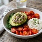 white ceramic bowl filled with tuna salad stuffed avocado half, scoop of cottage cheese, cherry tomato halves scattered all around