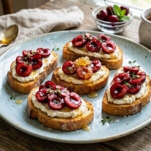 pale blue pottery plate with 5 slices of cherry ricotta toast drizzed with honey